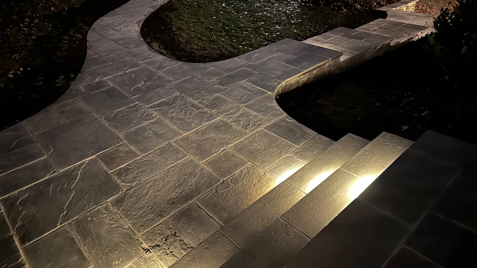 Landscape lighting installation around a fire pit and seating wall.